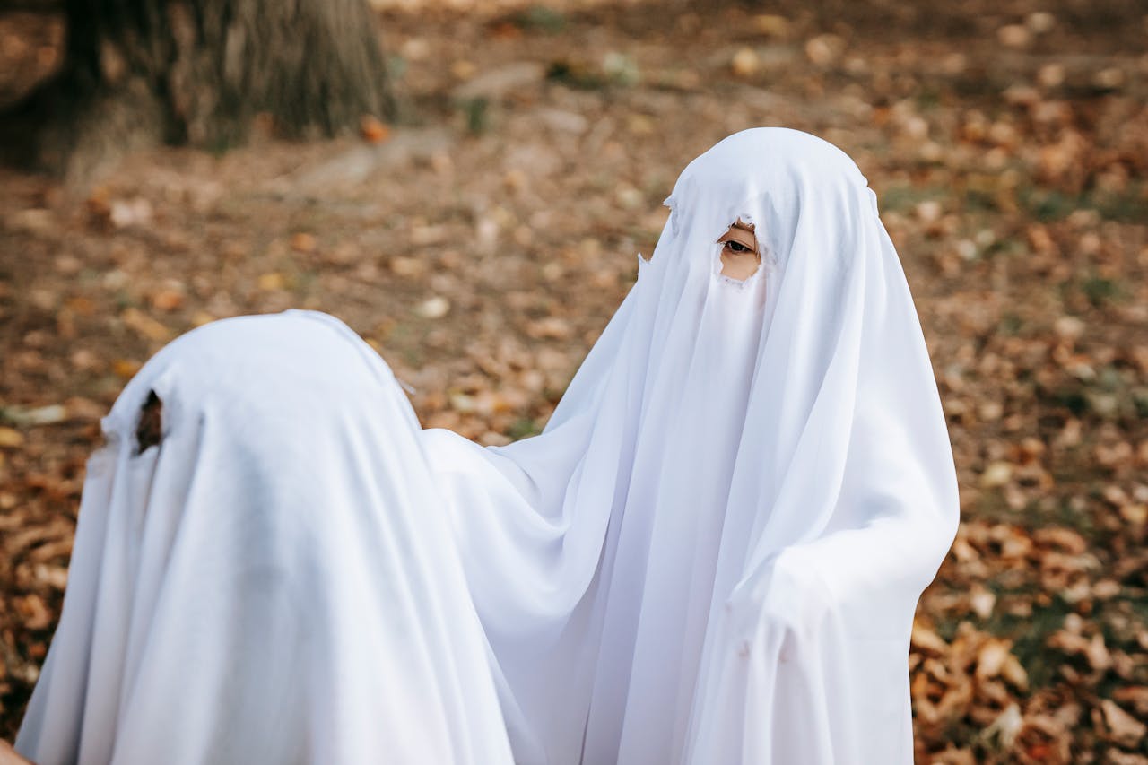 Children dressed as ghosts celebrate Halloween outdoors amidst autumn leaves.